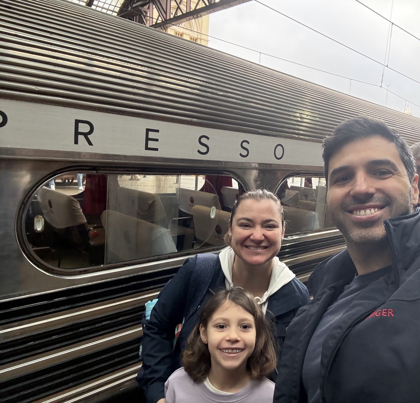 Claudia com a filha e o marido em frente a um trem na Estação da Luz