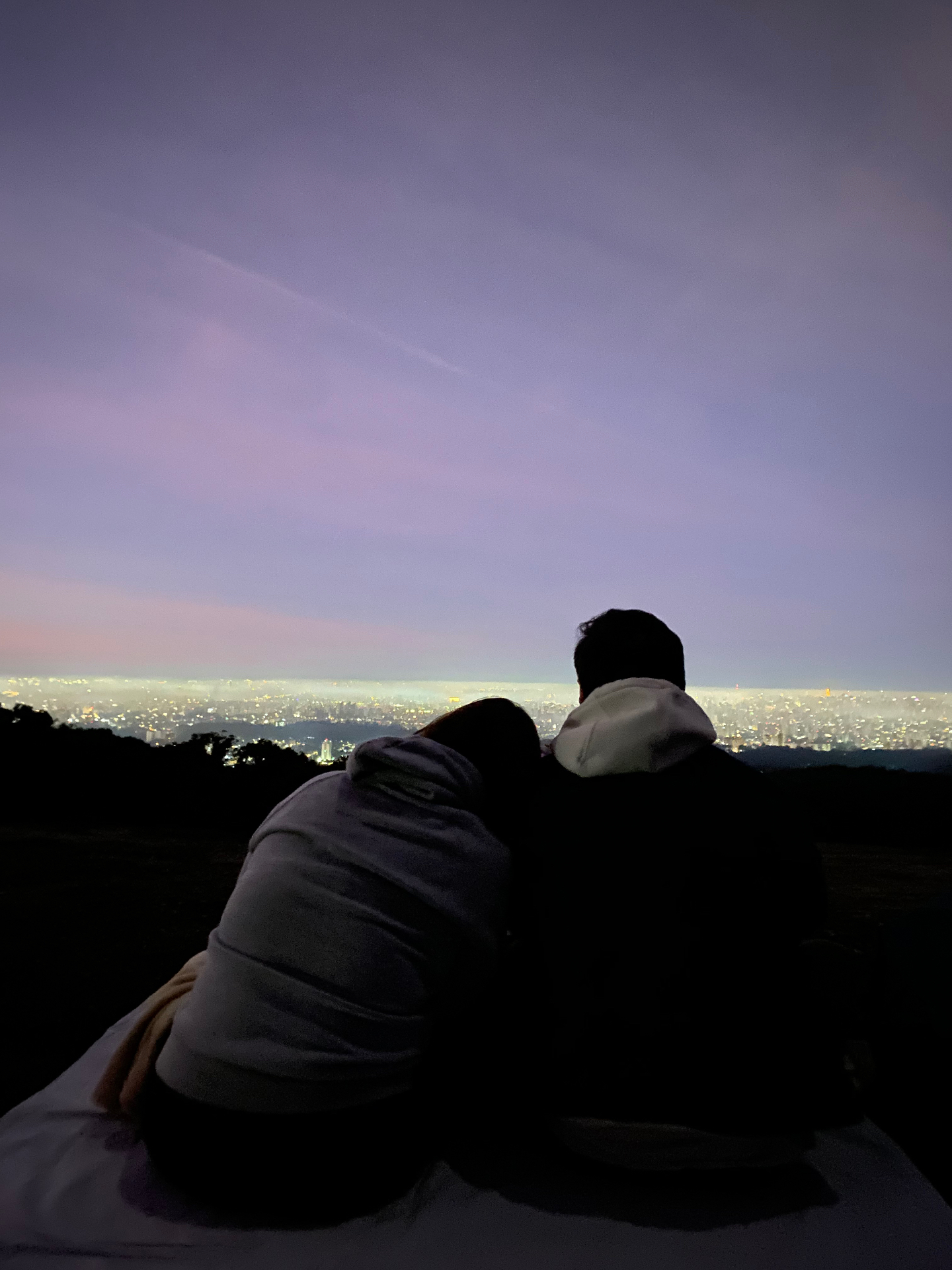 Casal abraçado admirando o pôr do sol sobre a cidade